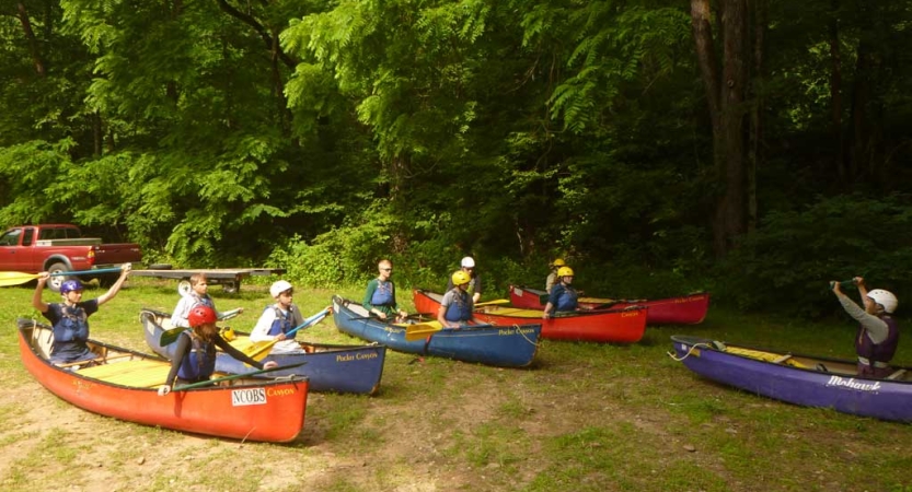 Students sit in canoes resting on the ground during instruction 